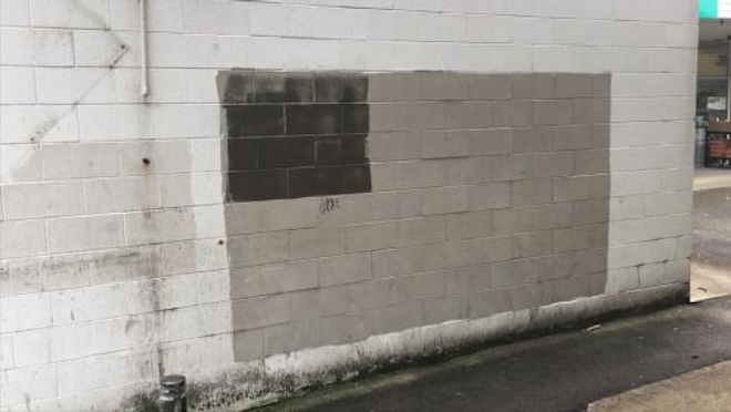 A white brick wall has two square shades of grey as if covering graffiti