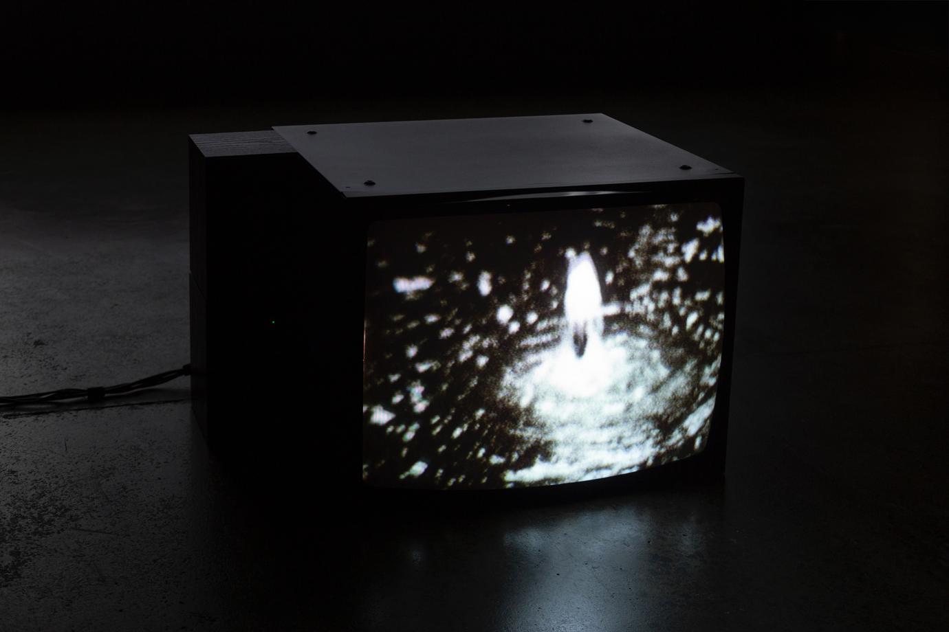 On a 4:3 cube video monitor we see a blurry black and white image of a fountain gushing upwards.