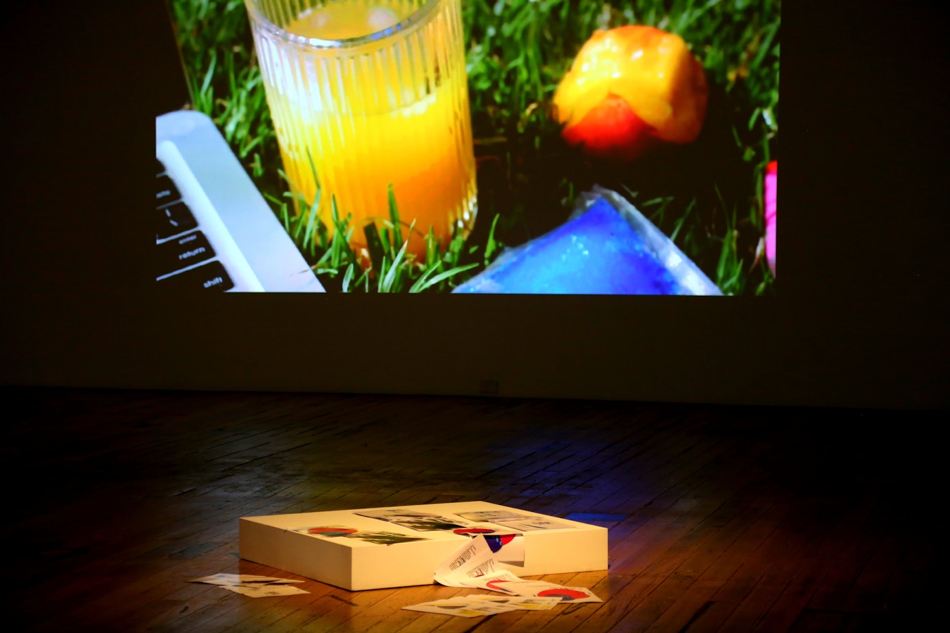 In the foreground a white block lies on the ground covered in scattered pages of images and text. In the background is a projection of the video Future Love