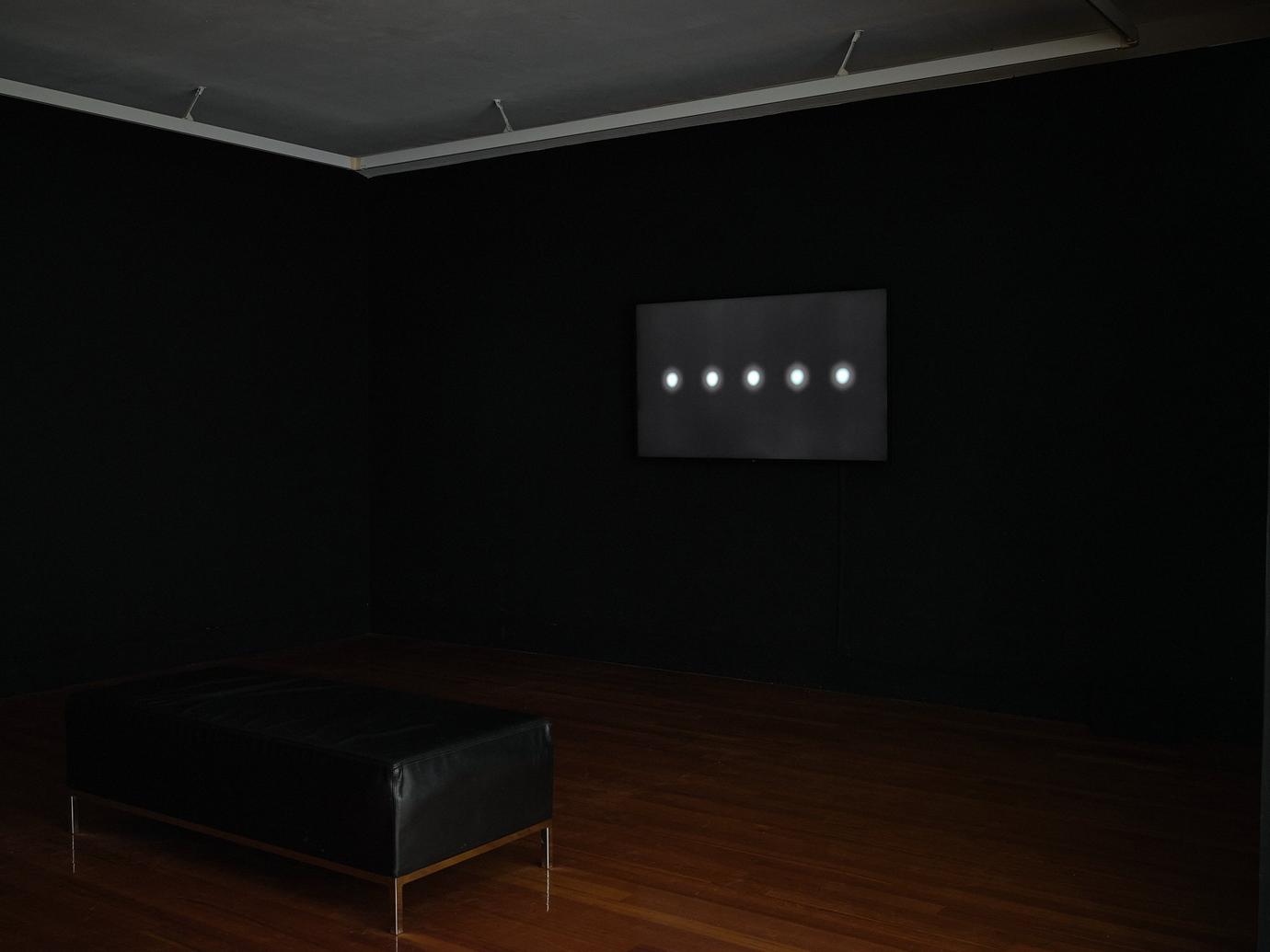 A black screen in a darkened room displays a horizontal row of five glowing white circles
