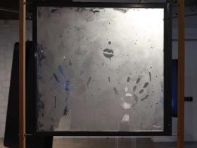 A steamy window in a wooden frame. There are two hand prints in the steam and a pair of lips.