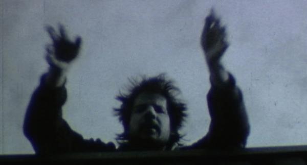A blurry image which shows a person with short dark hair leaning over a bridge or ledge. The person has their arms extended and looks as if they have thrown the camera over the ledge. Likewise it appears the camera has taken their photo. The colours are dark with high contrast. A blurry image which shows a person with short dark hair leaning over a bridge or ledge. The person has their arms extended and looks as if they have thrown the camera over the ledge. Likewise it appears the camera has taken their photo. The colours are dark with high contrast.