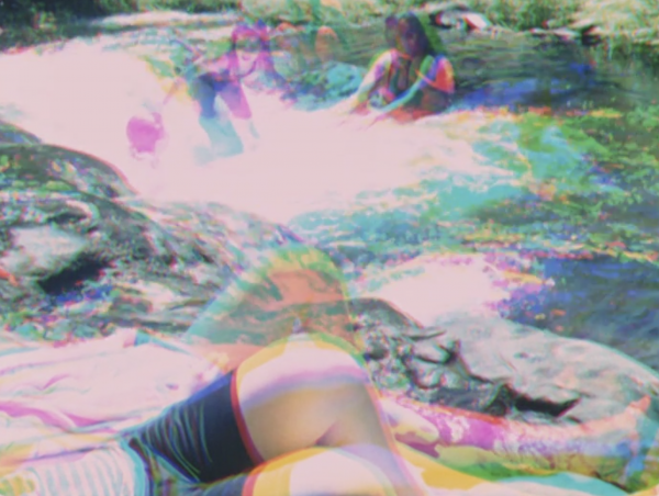 People play near a river or waterfall, laying near the water or swimming. The image has been made with a photographic technique called three colour separation, in which the scene is filmed three times, and each negative given a red, blue and green primary colour. These negatives are layered on top of each other, and combined into one image, which appears to show an ‘after-image’ of different movements recorded in each shot. People play near a river or waterfall, laying near the water or swimming. The image has been made with a photographic technique called three colour separation, in which the scene is filmed three times, and each negative given a red, blue and green primary colour. These negatives are layered on top of each other, and combined into one image, which appears to show an ‘after-image’ of different movements recorded in each shot.