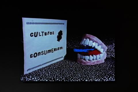 A pair of false teeth out of which pokes a blue tongue sits alongside a small sign that says 'Cultural Consumerism'.
