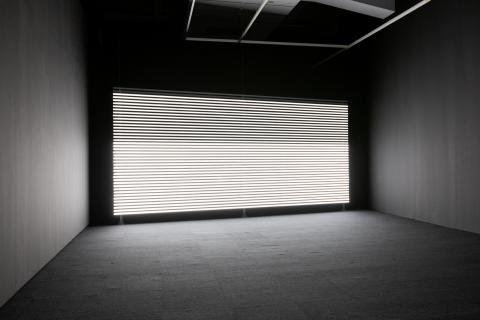Installation view of Marianna Simnett's work 'Faint with Light', showing a wall covered in horizontal bands of white light