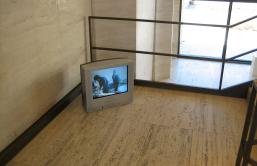 A small video monitor sits on the floor in the corner of what appears to be a stairwell. The monitor screen is in the early television ratio of 4:3, as opposed to the contemporary landscape format of 16:9. The monitor is an installation of Julian Dashper's video work Studio Songs (1998), installed at Sheldon Museum, Lincoln, Nebraska (2006).