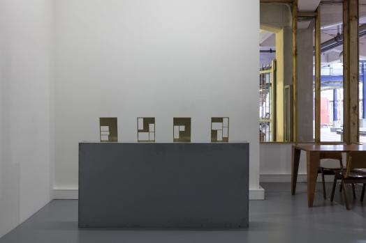 A plinth on which are five small artworks made of brass.
